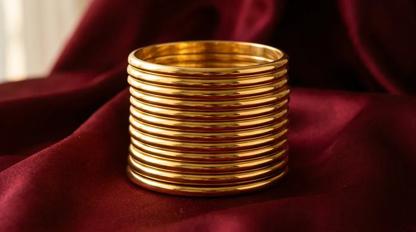 A stack of plain polished gold bangles resting on deep red silk under warm directional light