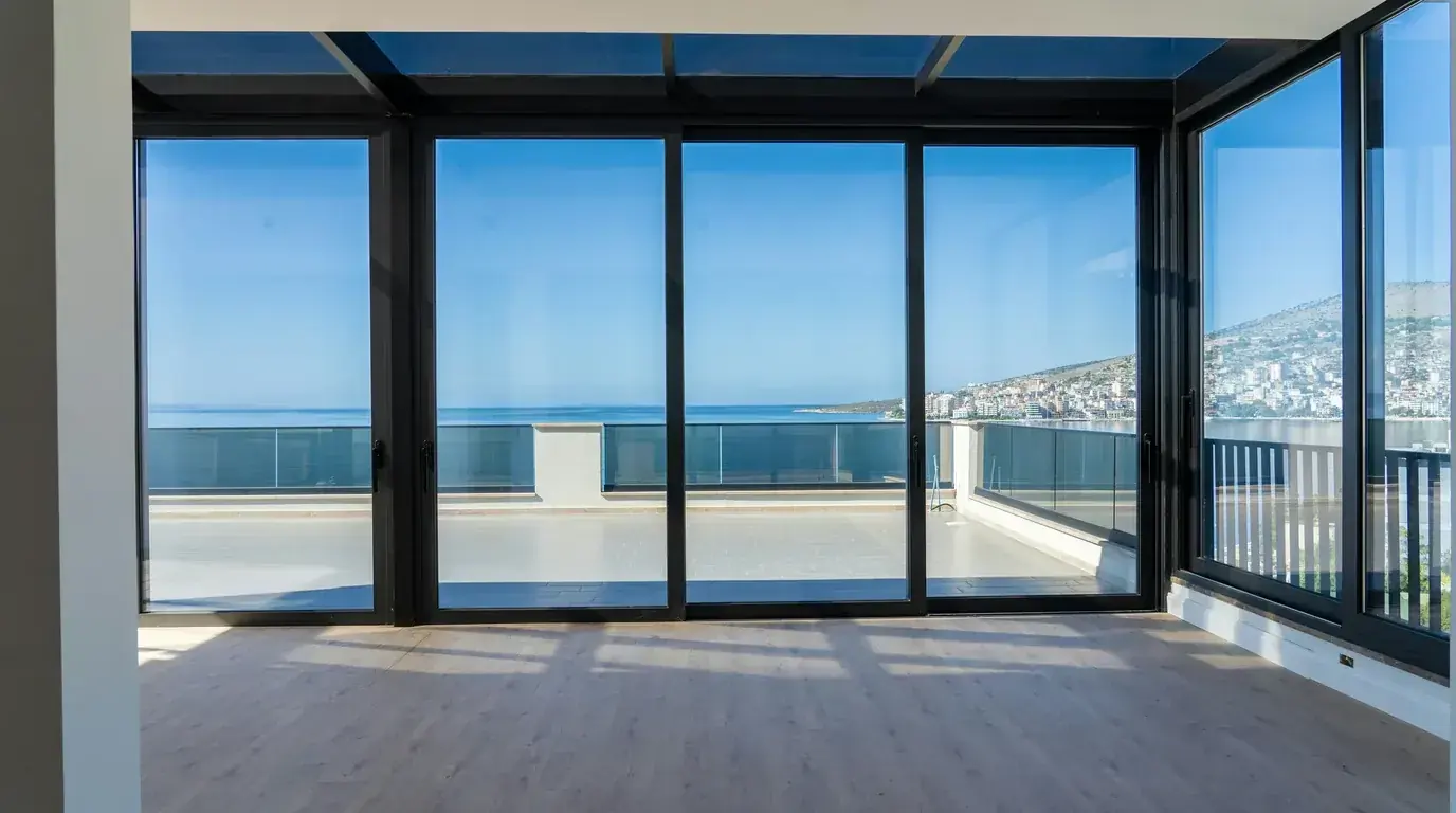 An empty room with sliding glass doors opening onto a balcony above the sea