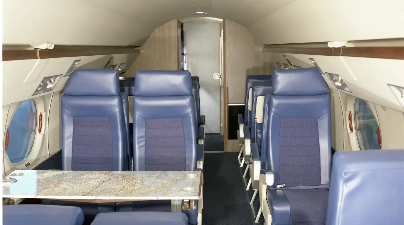 The cabin of a business jet: blue leather seats facing each other across a map-topped table, oval windows down both sides.