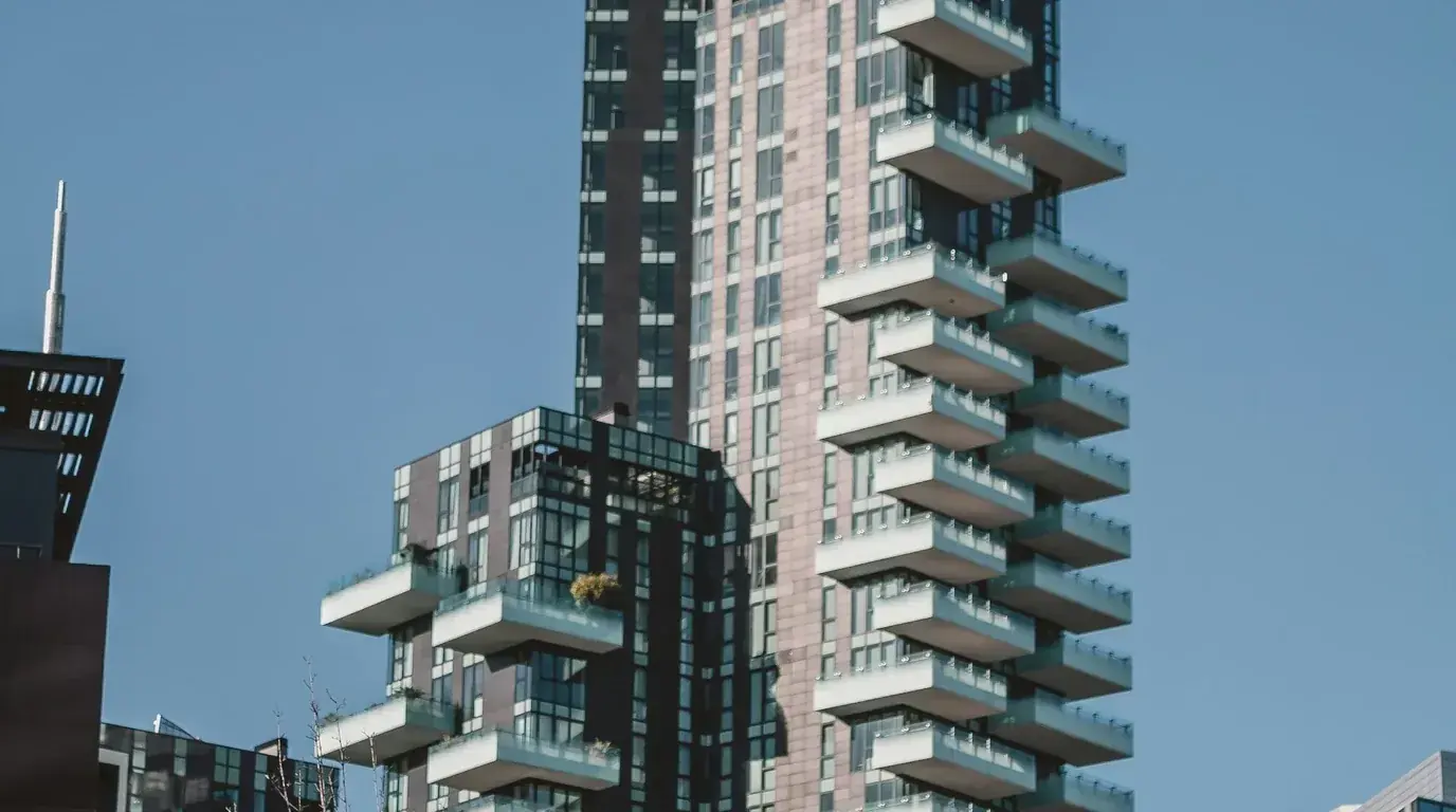 A residential tower with staggered cantilevered balconies against a clear sky, greenery on a few of them.